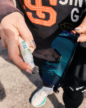 Person applying DFNS Eyewear Cleaner spray to their cycling sunglasses.