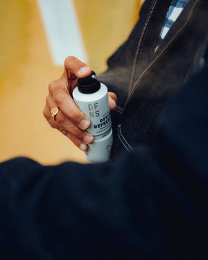Person spraying DFNS Denim Refresher on their denim jacket.